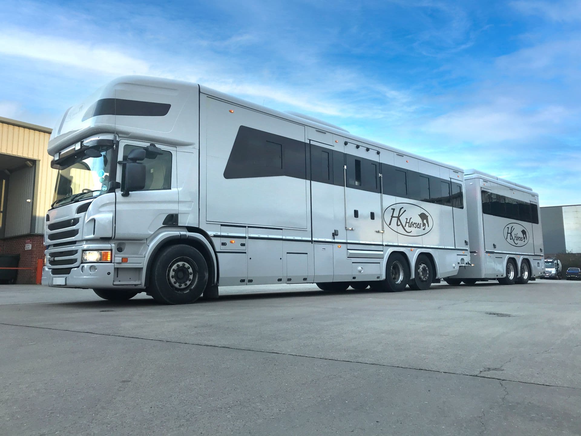 Large white Oatley Scania horsebox and trailer wrapped in gloss grey vinyl for HK Horses parked outside.